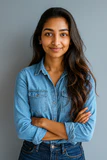 A professional headshot of Kavya Ramesh, a smiling woman with long dark hair, wearing a blue blazer, set against a neutral background, representing her role as Patient Care Manager at Dezy.